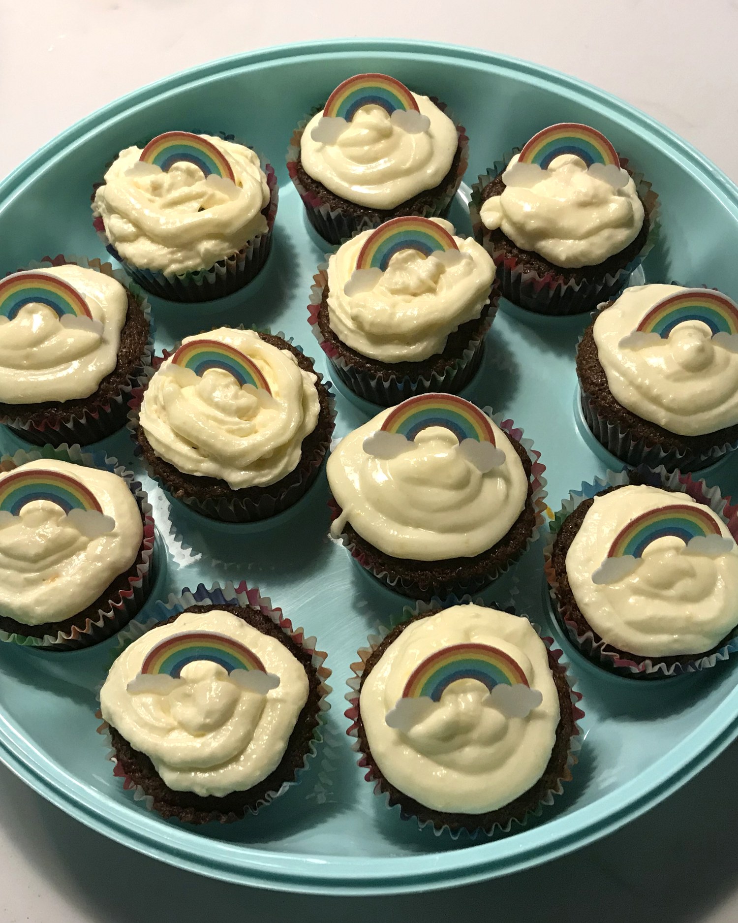 Carrot cupcakes with swirled cream cheese frosting, each finished with a little rainbow-and-cloud sugar topper, on a pale blue plate.